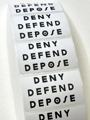 Roll of white rectangular stickers repeatedly printed with the words 'DENY DEFEND DEPOSE' in black.