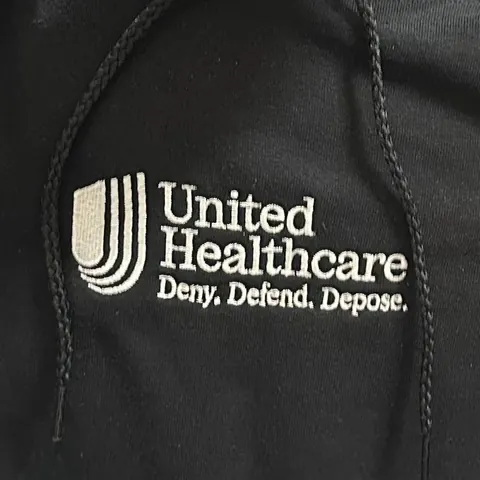 Close-up of black fabric embroidered with a UnitedHealthcare-style logo and the added phrase 'Deny. Defend. Depose.' beneath it.