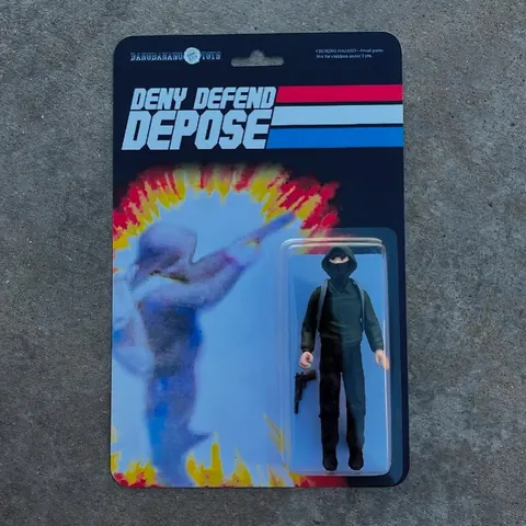 Mock action-figure blister package labeled 'DENY DEFEND DEPOSE,' containing a small dark-clothed figure beside a stylized explosion graphic.