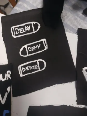 Black card or print showing three outlined bullet shapes labeled 'DELAY,' 'DENY,' and 'DEPOSE' in white lettering.