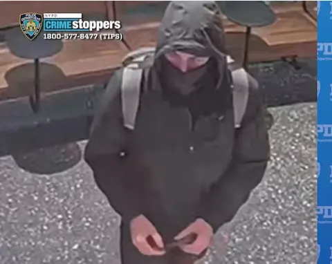 CCTV-style still showing a hooded person in dark clothing with backpack straps visible, photographed from above, with NYPD Crime Stoppers branding in the upper-left corner.