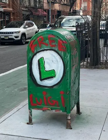 A green-painted street mailbox marked 'FREE' and 'LUIGI' in red, with a large white circle containing a green letter L on the front.