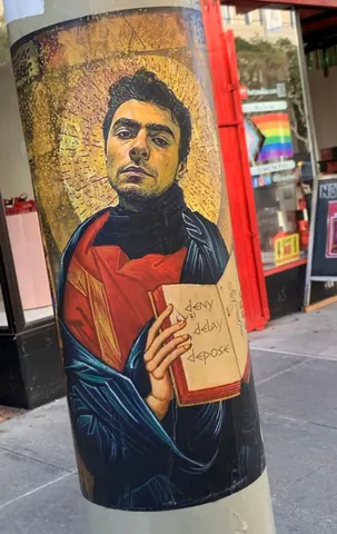 Painted portrait on a street pole showing a young man in red holding a small paper marked with faint 'deny defend depose' text.