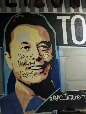 Painted portrait mural of a man with black handwritten 'Deny Defend Depose' text across the face and a circled-A symbol beside it.