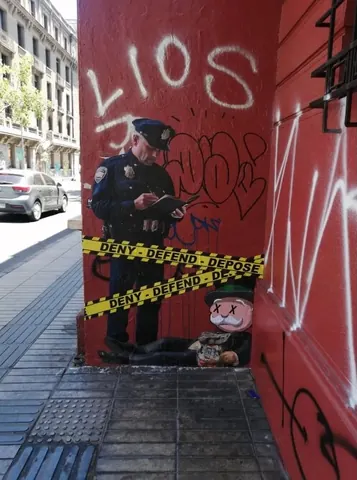 Street-art installation on a red graffiti-covered wall showing a pasted figure with yellow-and-black bands repeating 'DENY DEFEND DEPOSE' across the lower half.