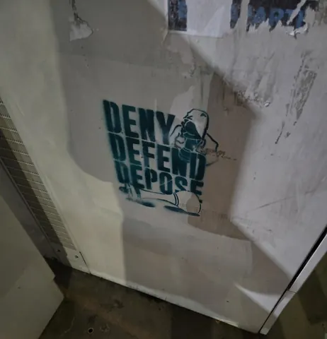 Dark teal stencil on a light wall reading 'DENY DEFEND DEPOSE' beside a small stylized figure.