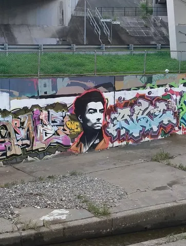 Street mural on a low wall showing a large painted portrait of a young man in a red-orange top amid colorful graffiti.