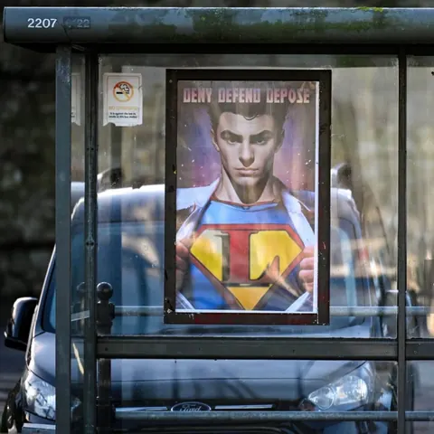 Poster displayed inside a bus shelter depicting a young man in a Superman-like costume, with 'DENY DEFEND DEPOSE' printed across the top.