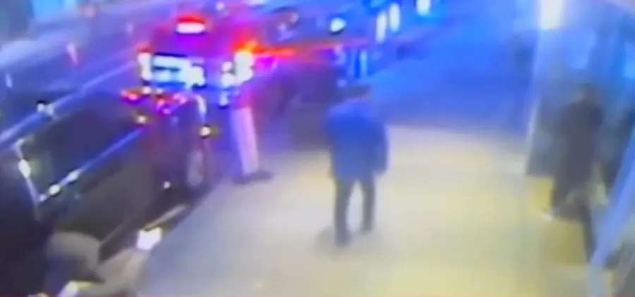 Blurry nighttime surveillance frame showing a person near a brightly lit vehicle.